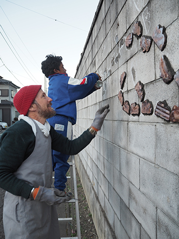 A man in a winter hat and his young son affix tiles on a wall