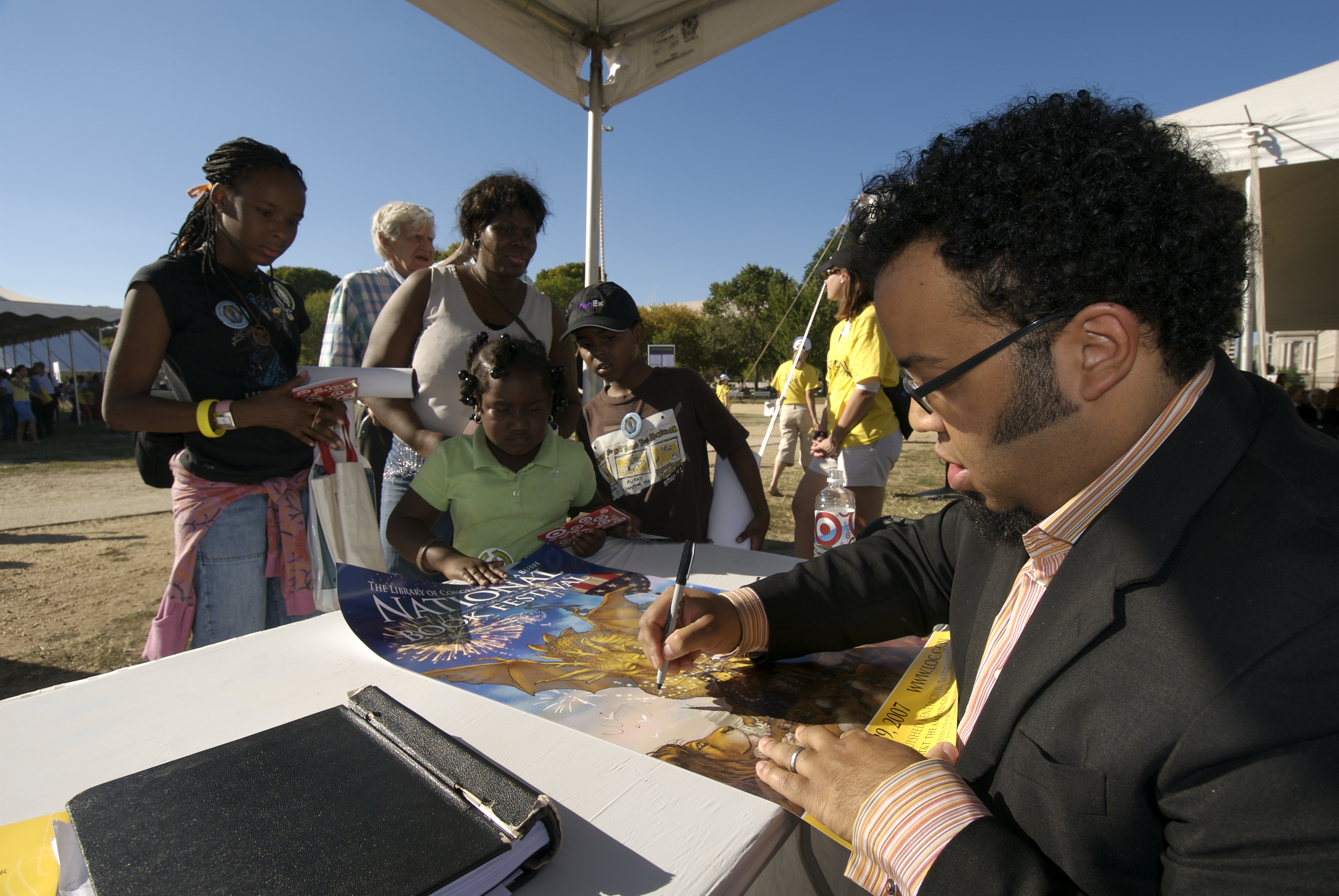 Kevin Young signing a poster with kids standing around him.