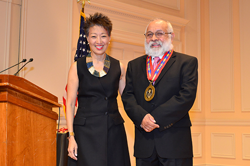 Woman in black dress next to man in suit with medal around his neck. 