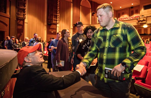 Readers lined up in auditorium with copies of The Things They Carried. Tim O’Brien shakes hand of one young man.