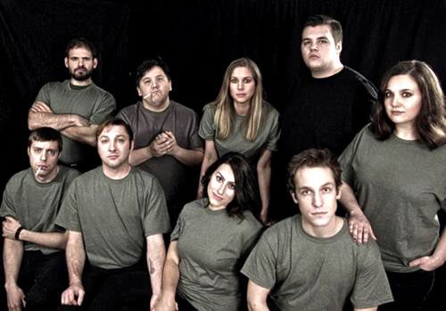 Nine students in grey shirts and stage makeup stand in front of a black backdrop