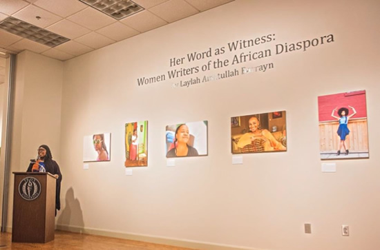 Woman stands at podium, five photographs featuring black women displayed behind her.