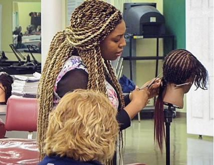 Woman demonstrates weave process on mannequin head.