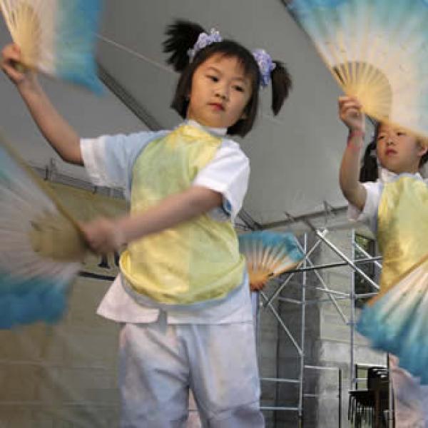  two young girls in festive costume dancing with multi-colored fans