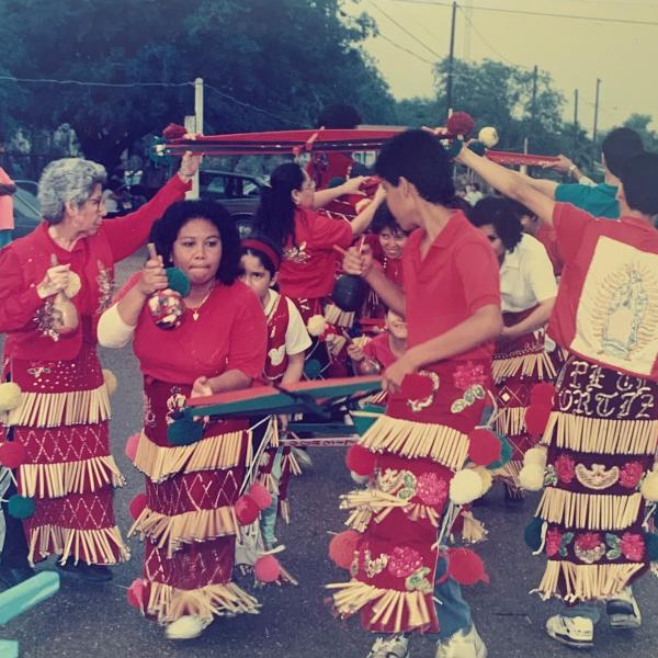 Group of women in colorful red outfits dancing in the street. 