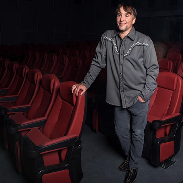 Man standing while holding onto red theater seats