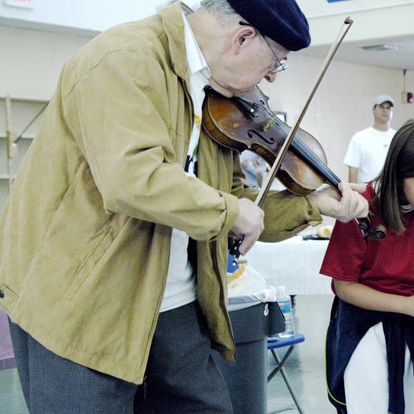 An elderly man playing violin to a couple of children.