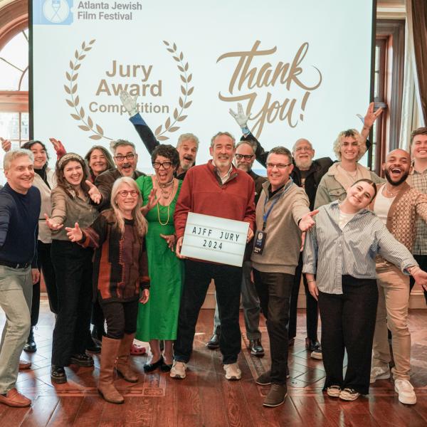 Photo of a group of people holding their arms out in celebration and smiling in front of a projector that says “Atlanta Jewish Festival,” “Jury Award Competition,” and “Thank You!”