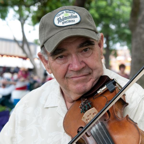 Man in baseball cap playing fiddle outdoors