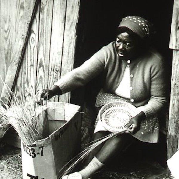 A woman making a wicker basket on her door step.