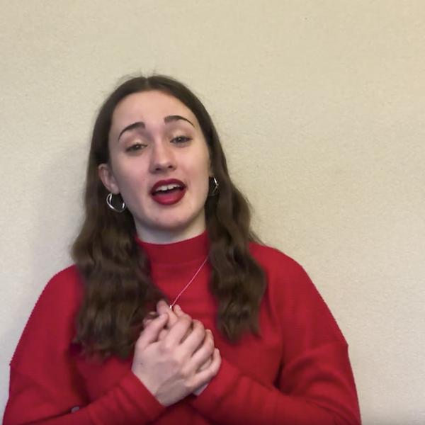 Woman in red sweater holds hands to chest as she recites to camera