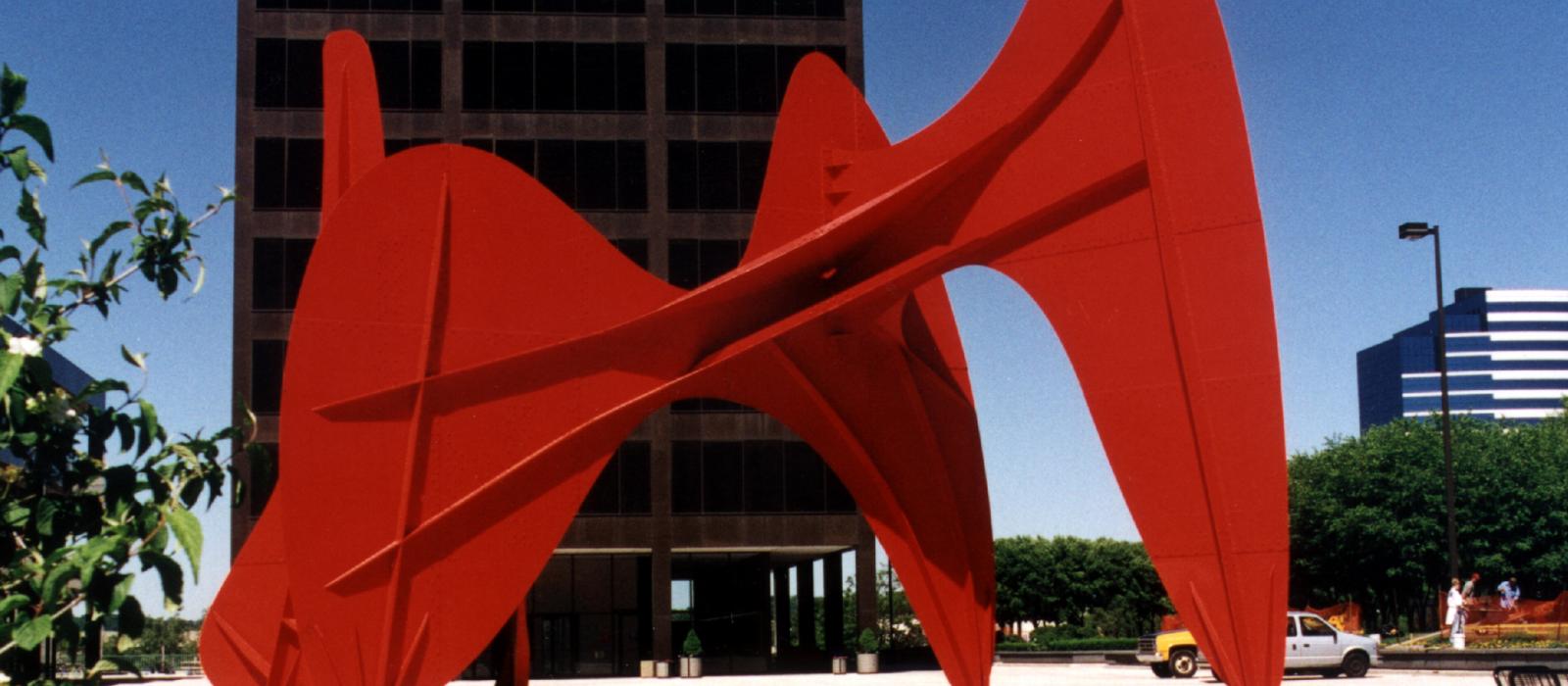 Large red abstract artwork in city square.