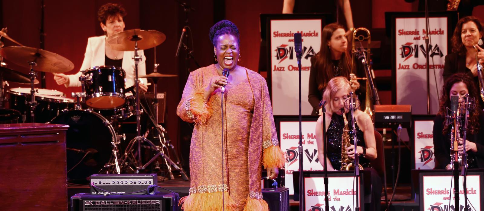 Woman in orange dress singing in front of an all-women jazz orchestra