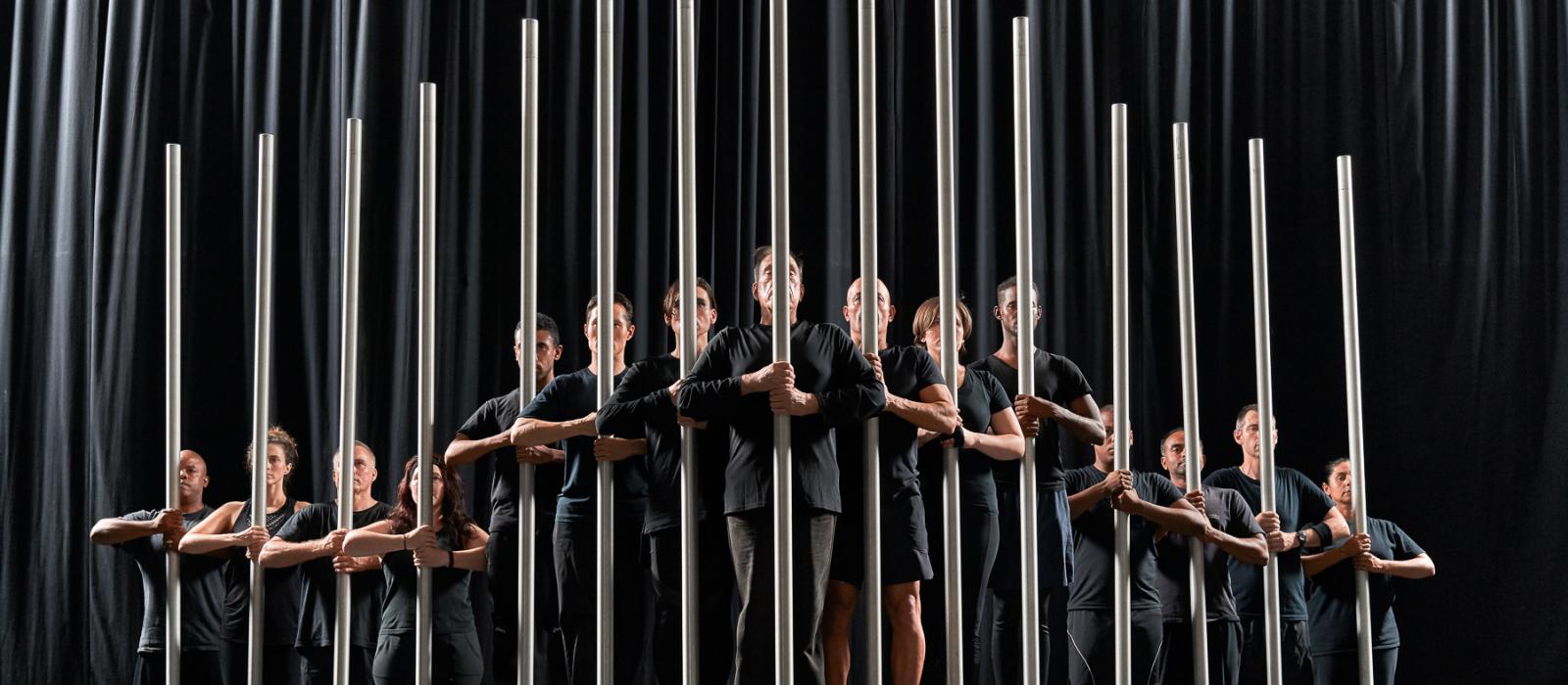 Men and women in black holding poles on stage.