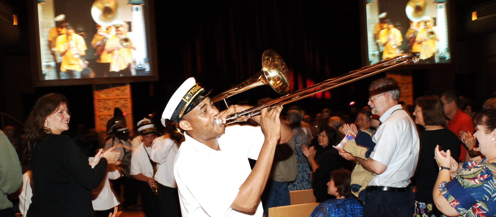 Trombonist walking through aisle of performing arts center.
