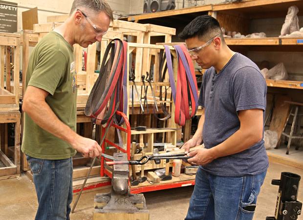 Two men in a metalworking workshop working together to shape a hot piece of metal