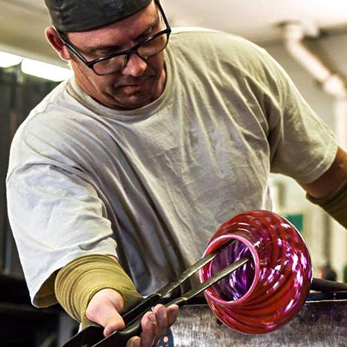 Man holding a hot glass vessel with glassblowing forceps