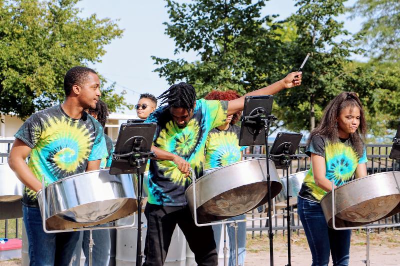 Three people in tie-dye shirts play steel drums at an outdoor venue