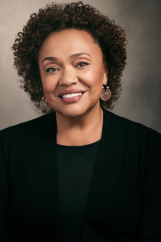Black woman smiling and wearing a black sweater in front of a grey and black watercolor backdrop