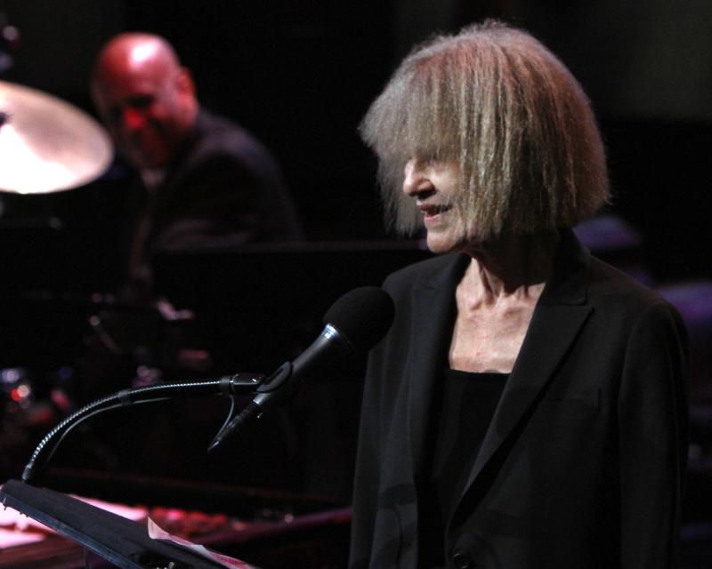 Carla Bley stands behind a microphone