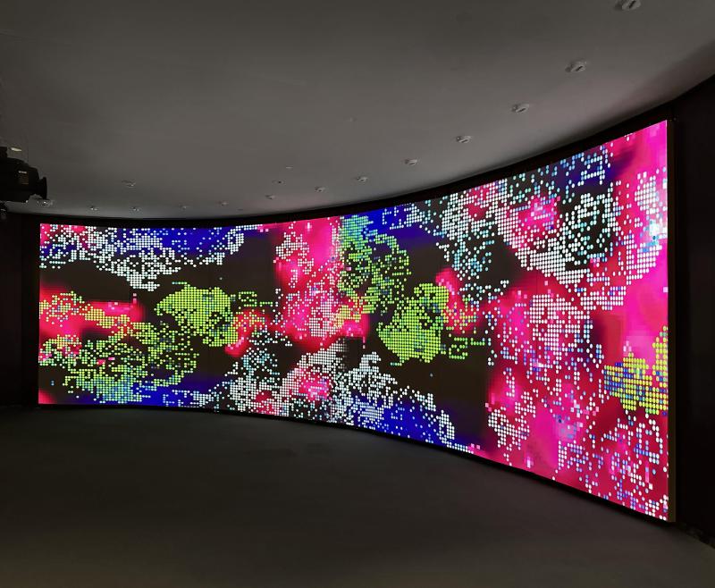 Multi-colored (blue/green/pink/black/white) abstract on a large video display.