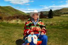A man in a cowboy hat and colorful jacket sits in an open field.