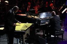 A man performs on the vibraphone next to another man performing on the piano.