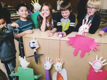 Several children pose with "people" made out of inflated latex gloves and paper