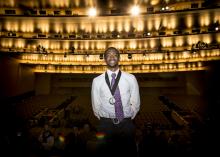 a young black man stands on a stage with back to audience and halo of stage lights