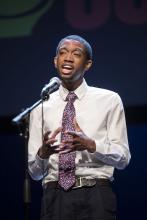 a young black man with short hair recites into a microphone