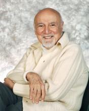 A man in a white sweater sits in a chair facing the camera