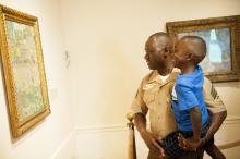 father holds son as both look at a painting in a museum