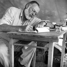 Ernest Hemingway sitting at a table and writing. 