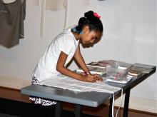 A young girl bends over and decorates an apron as part of an exhibition