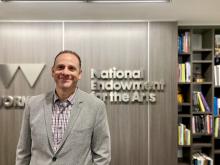 man smiling in front of National Endowment for the Arts sign