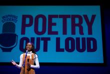 A young woman speaks at a microphone with the Poetry Out Loud logo on a screen behind her.
