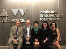 2 white men, an asian woman, and 2 white women  sit on a bench against a background that has the NEA  logo