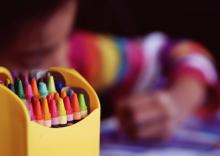 a photograph which highlights a box of crayons next to a child in the background