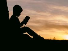 Silhouette of young boy reading a book against the sunset