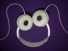 white headphones placed upside down on a purple background so they look like a smily face