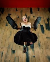An Asian woman in a black velvet dress lying on the wooden floor with a pig on each side of her. 