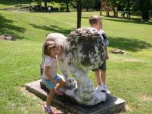 two young children play around a stone lion outdoors