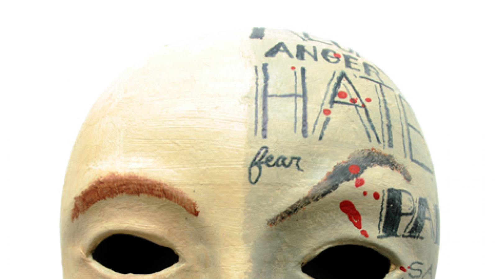 A paper mache mask painted with the words 'hate,' 'guilt,' and 'remorse.'