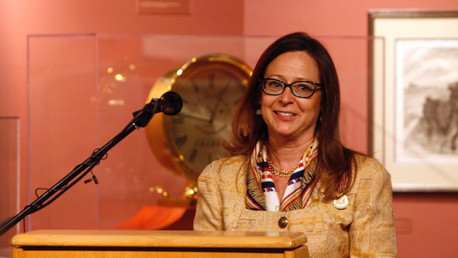 a brown-haired woman with glasses stands behind a podium