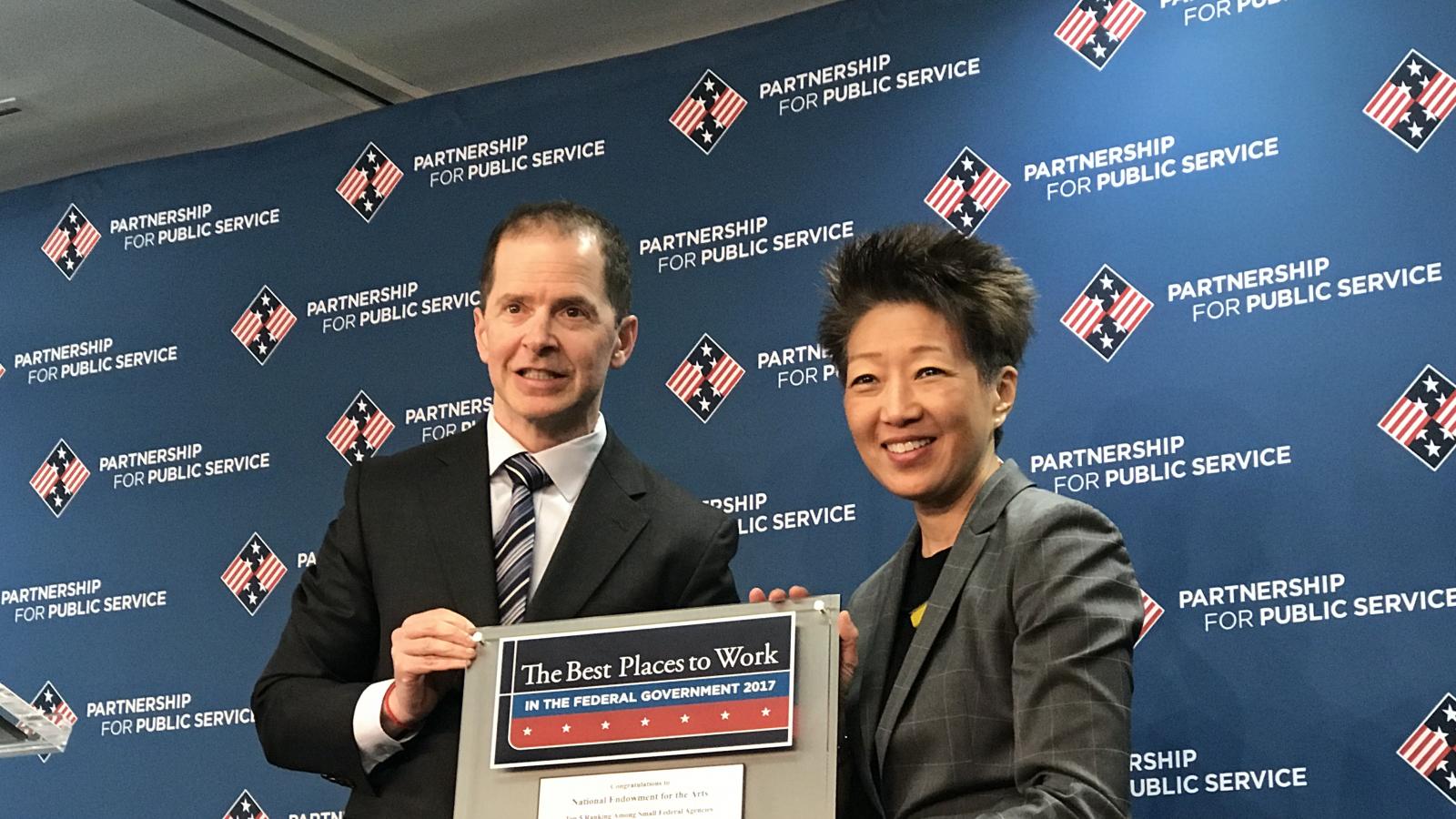 A man and a woman pose holding a plaque which says "The Best Places to Work in the Federal Government 2017"