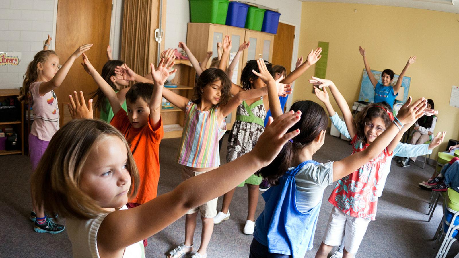 Young children raise their hands above their heads as they take part in a dance class