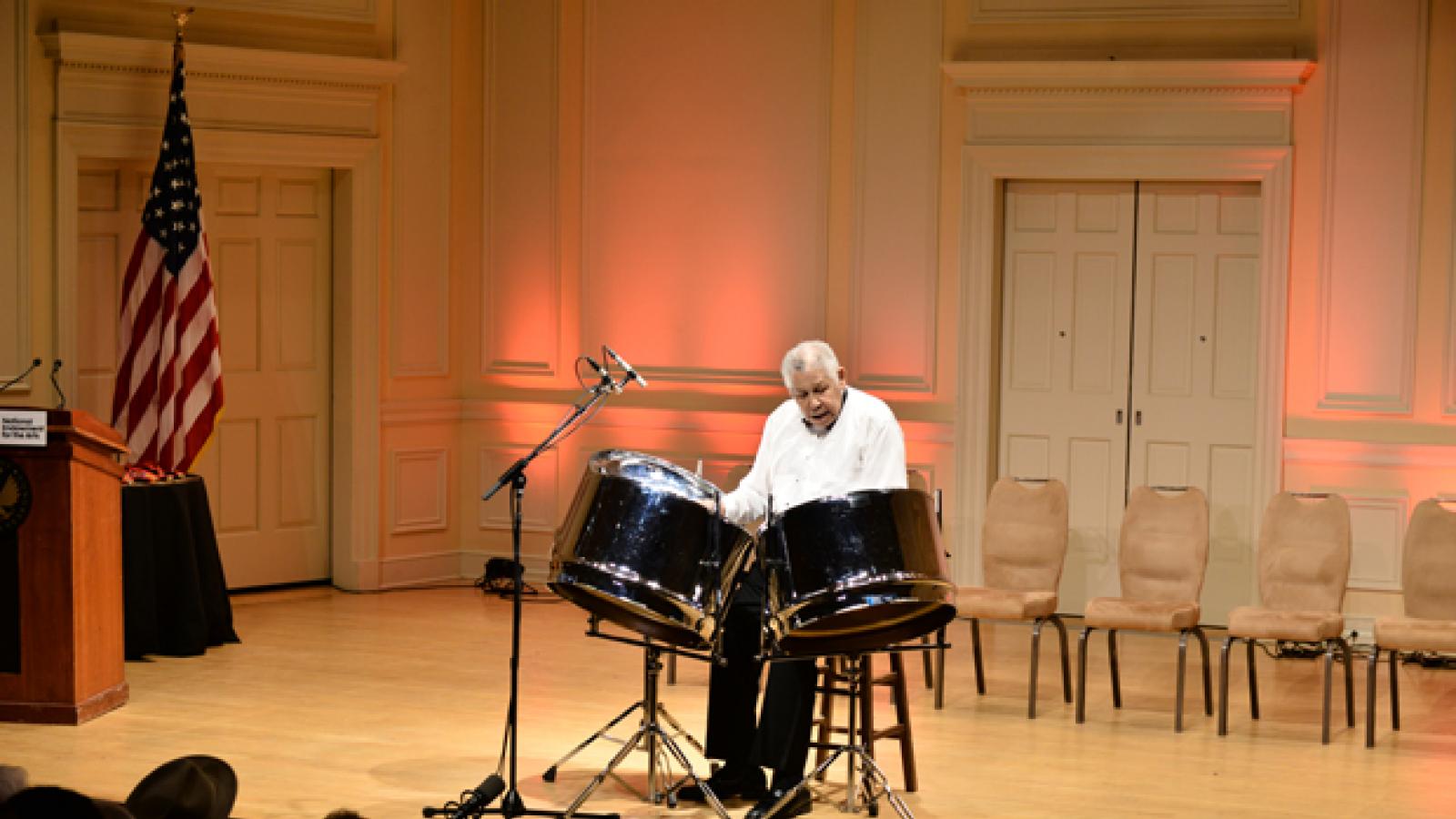 A man sits on a stage behind three steel drums