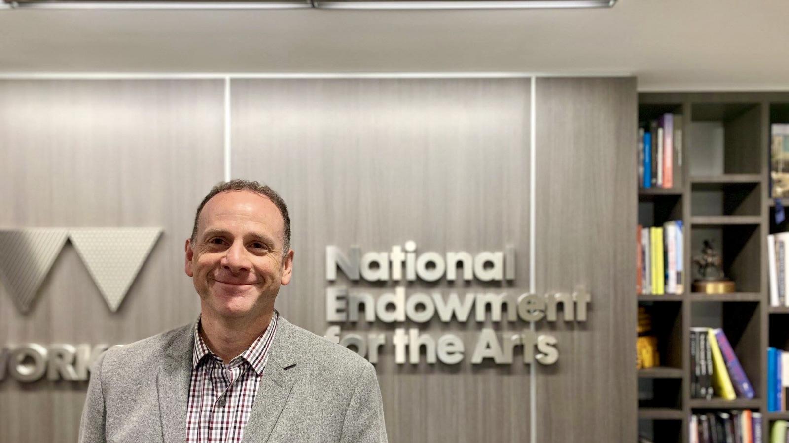 man smiling in front of National Endowment for the Arts sign