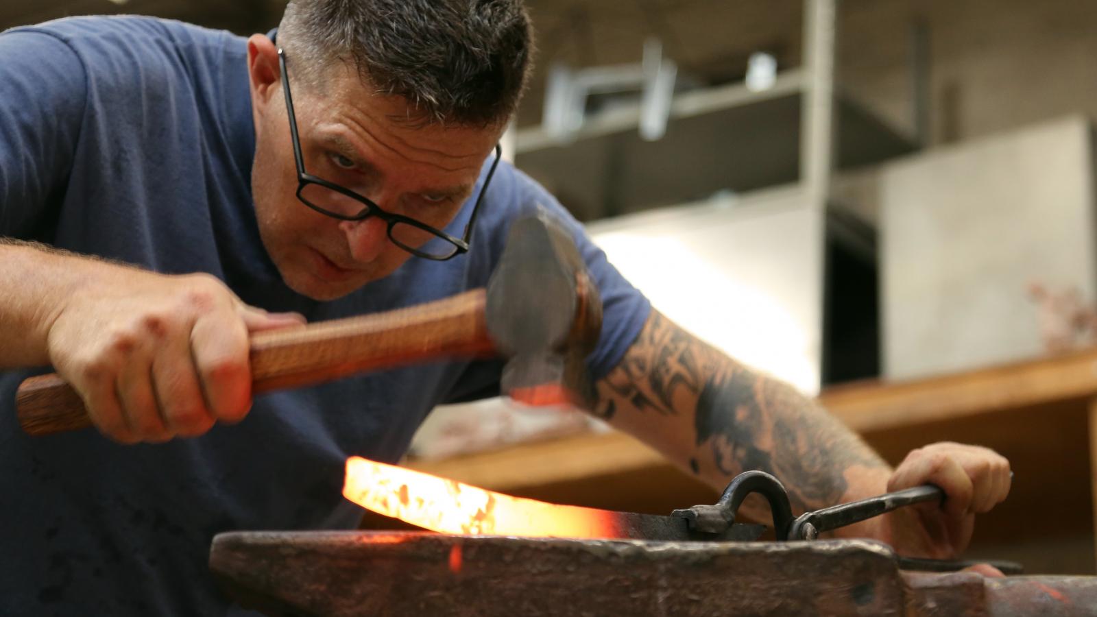 Man looks closely at a blade he is forging