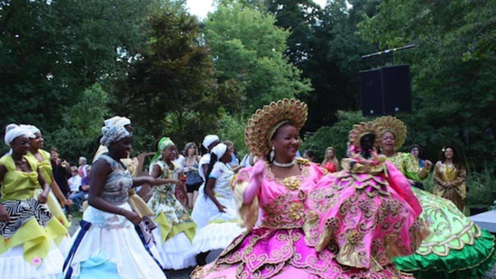 a parade of women in brilliantly colored costumes featuring wide hoop-like skirts that are heavily decorated
